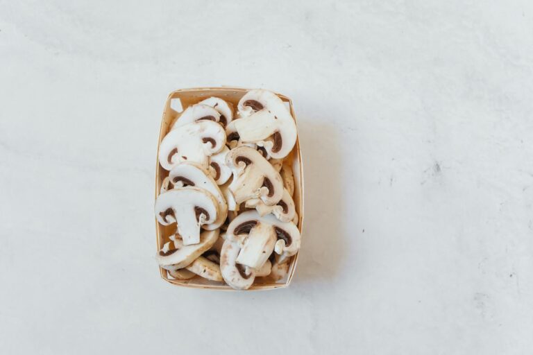 Overhead shot of fresh sliced champignon mushrooms in a box on a light surface.